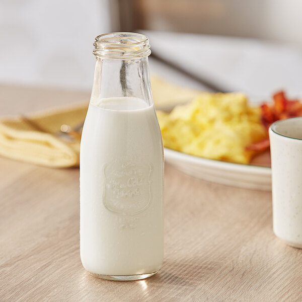 An Acopa glass milk bottle filled with milk on a white surface.