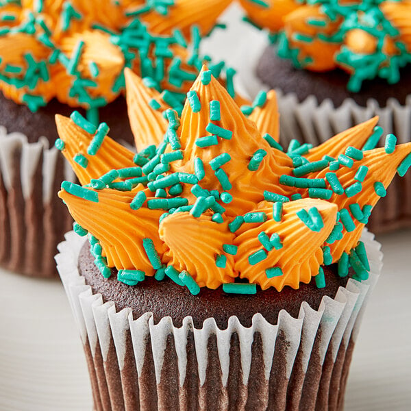 A close up of three cupcakes with orange frosting and green sprinkles.