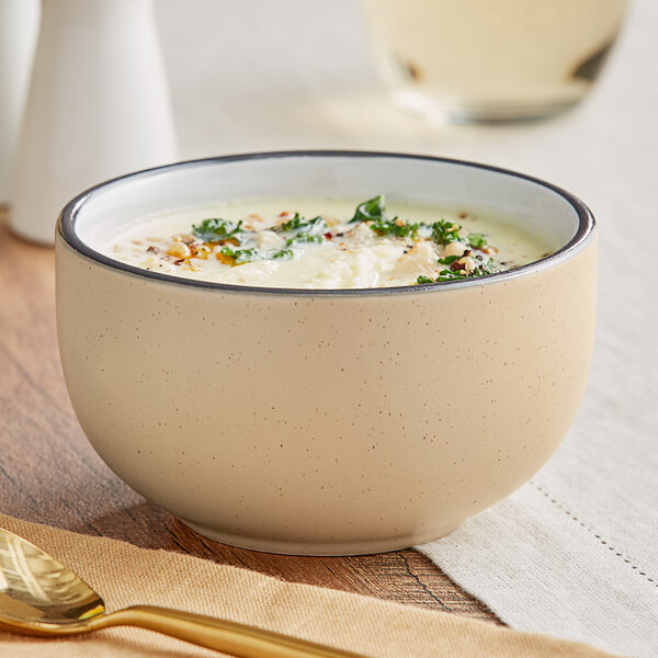 An Acopa Harvest Tan stoneware bowl filled with soup on a table with a spoon and a glass of wine.