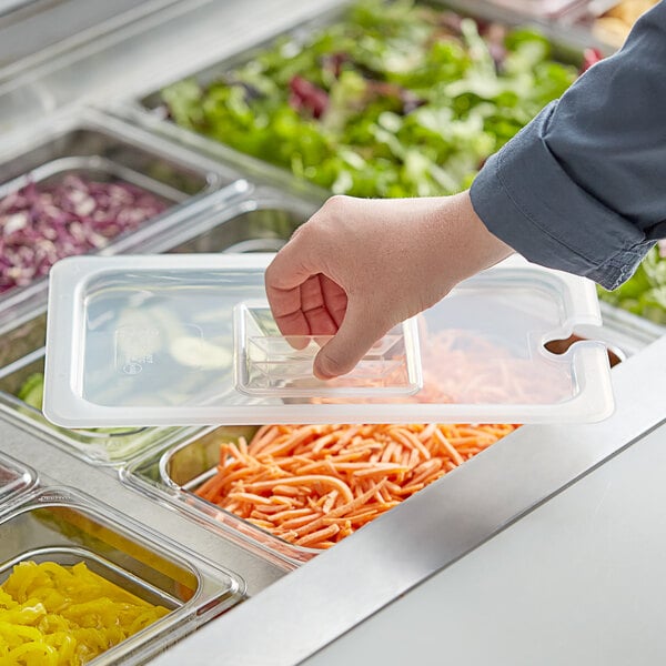 A hand using a Vigor translucent polypropylene handled lid to cover food in a plastic food pan on a counter.
