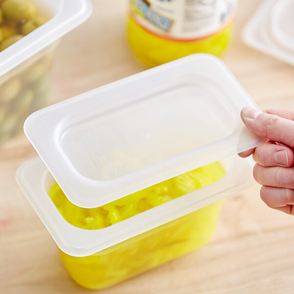 A hand placing a Vigor translucent polypropylene lid on a plastic container of yellow food.