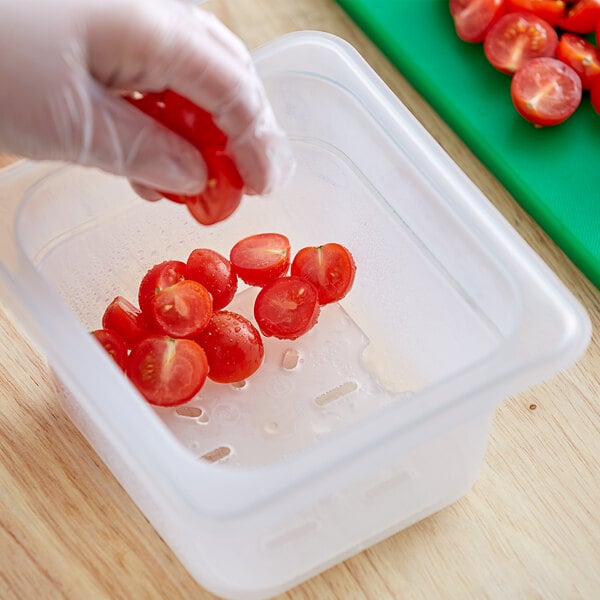 A person in gloves uses a Vigor translucent polypropylene drain tray to hold tomatoes while cutting.