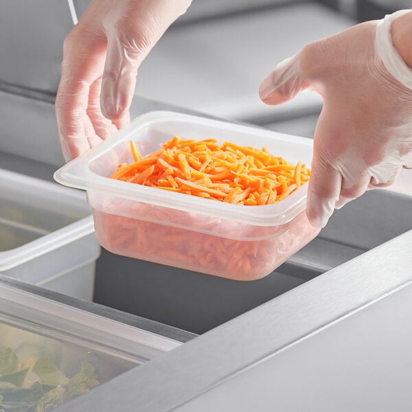 A person in gloves holding a Vigor translucent plastic container of shredded carrots.
