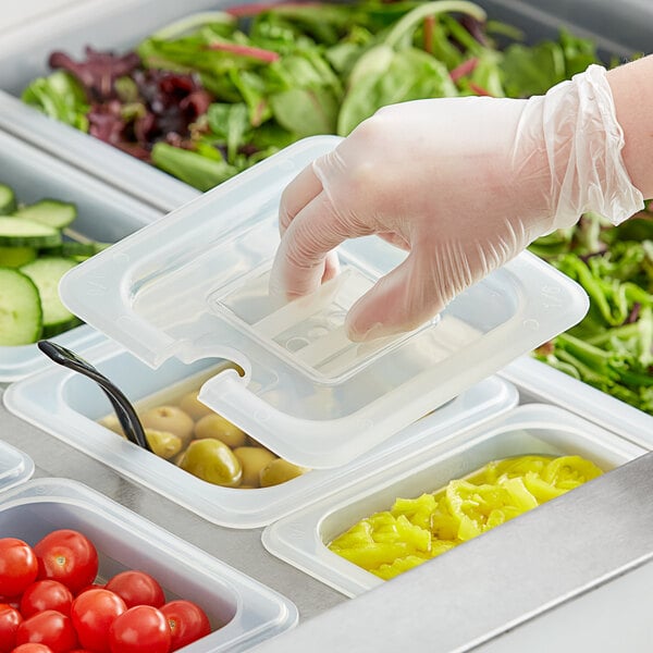 A hand in a plastic glove using a Vigor translucent plastic lid to cover a container of food.