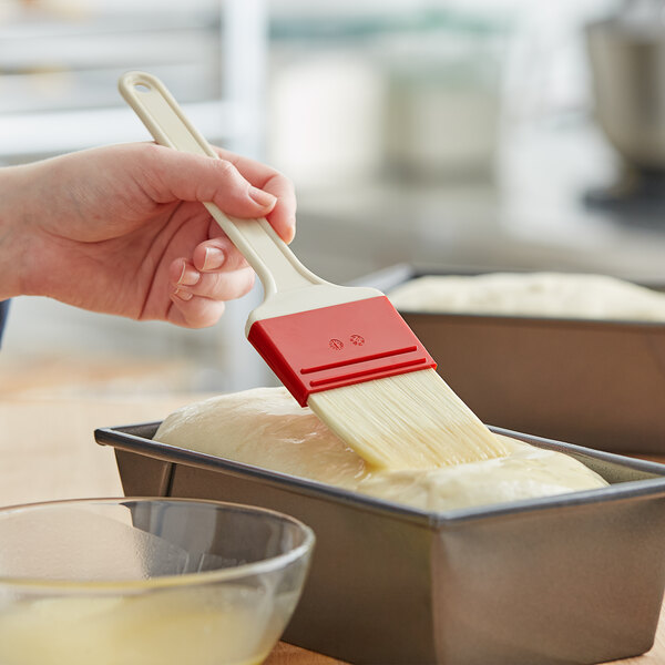 A person using a Thermohauser pastry brush to spread egg wash over a loaf of bread.