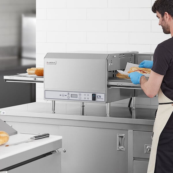 A man using a Lincoln 50" Ventless Electric Countertop Conveyor Oven to make a sandwich.