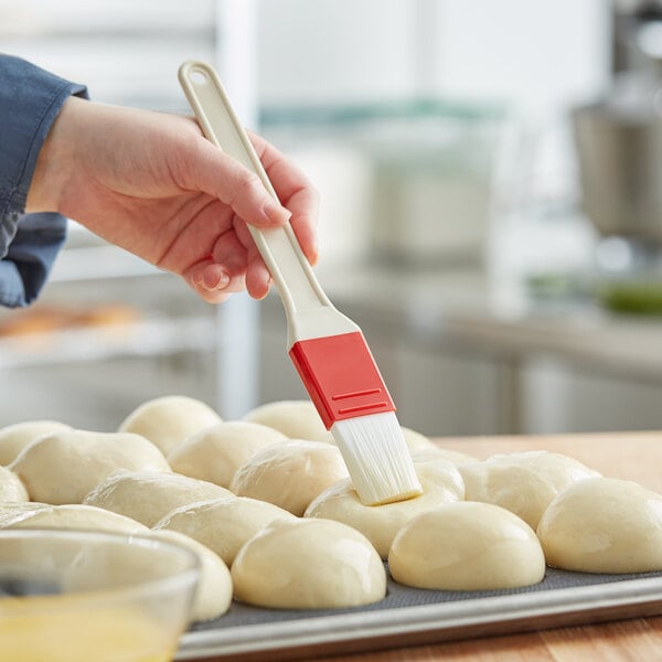 A person using a Choice white and red pastry brush to baste dough.