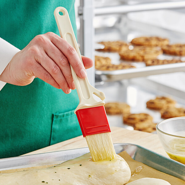 A person using a white and red Choice pastry brush to spread dough on a tray.
