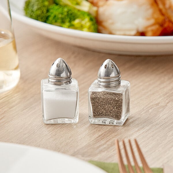 An American Metalcraft salt shaker with a metal top on a table with a plate of food.