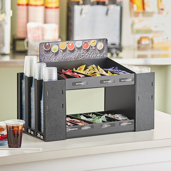 A black ServSense condiment organizer with cups and lids on a counter.