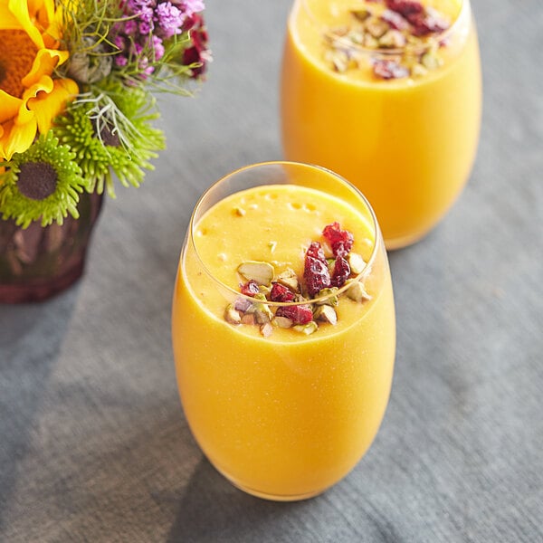 Two glasses of Ashoka Kesar Mango pulp drinks with dried fruit and nuts.