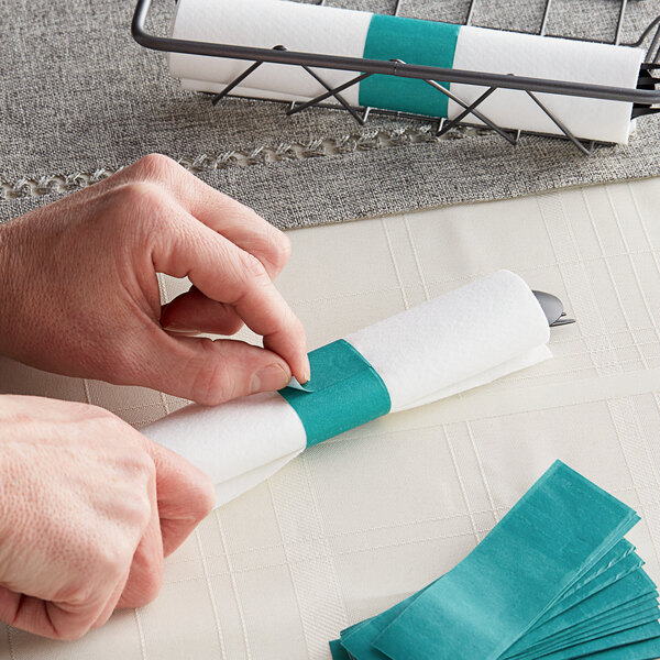 A person's hands wrapping a stack of paper napkins with teal bands.