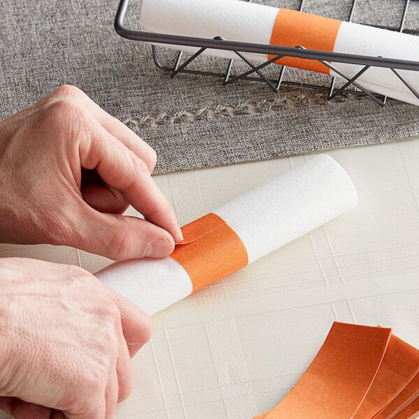 A person using a Rust paper napkin band to roll a paper napkin.