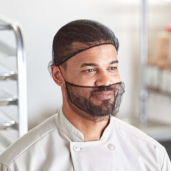 A man in a chef's uniform wearing a black net hairnet over his head.