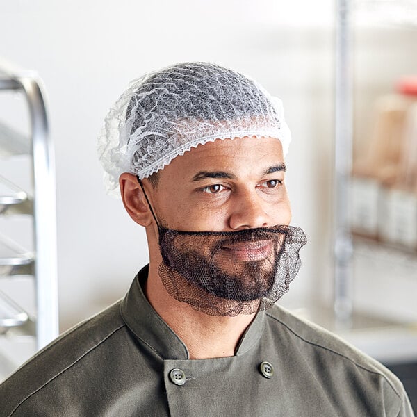 A man wearing a white pleated bouffant cap on his head in a professional kitchen.