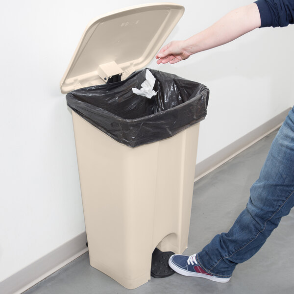 A person using their foot to open a Continental beige rectangular trash can.