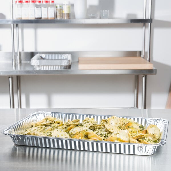 A Western Plastics foil steam table pan filled with food on a table.