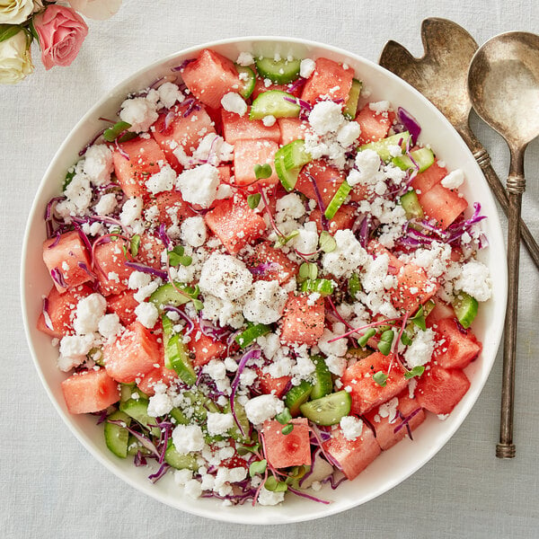 A bowl of watermelon salad with crumbled vegan feta cheese and cucumbers.
