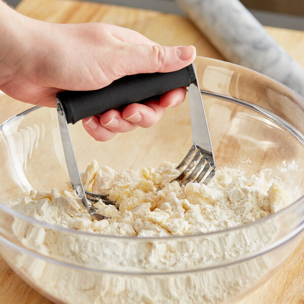 A person using a Choice stainless steel pastry blender with a black non-slip handle to mix flour.