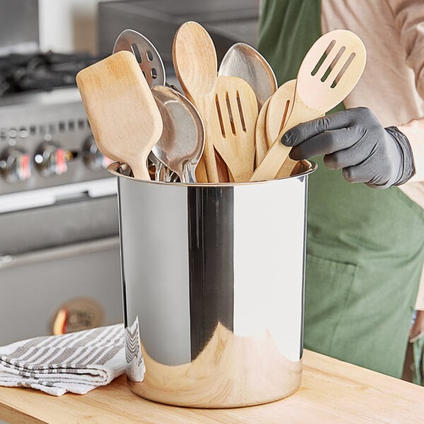 A silver stainless steel container holding wooden and metal utensils including a spoon and wooden spoon.