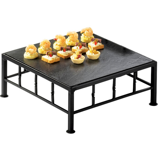 A Cal-Mil black metal square riser with food on a slate tray.