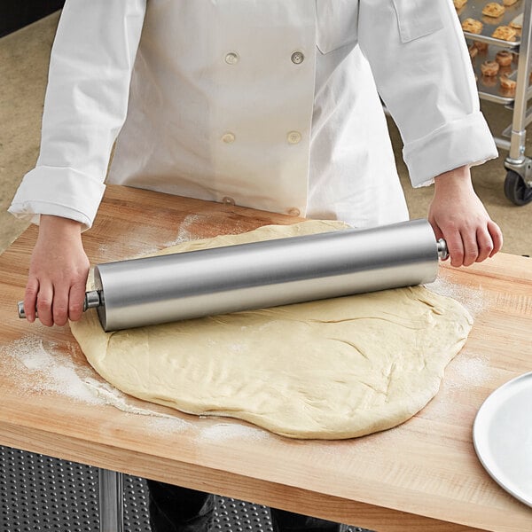 A person in a white coat rolling out dough with a Choice aluminum rolling pin.