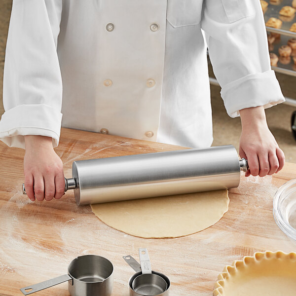 A person using a Choice aluminum rolling pin to roll out dough on a table.