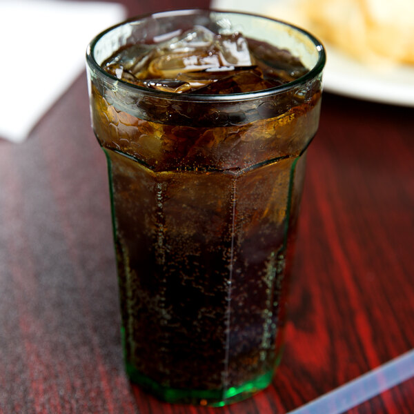 A Cambro Spanish Green plastic tumbler filled with soda and ice with a straw.
