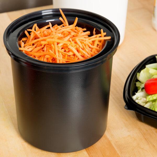 A black Cambro ColdFest crock filled with shredded carrots on a table with a salad.