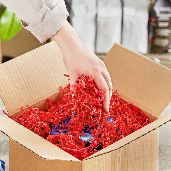 A person's hand holding a box with Spring-Fill red crinkle cut paper shred.