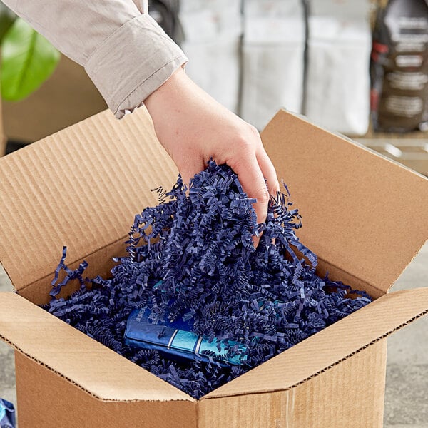A hand holding Spring-Fill navy blue crinkle cut paper shred in a cardboard box.