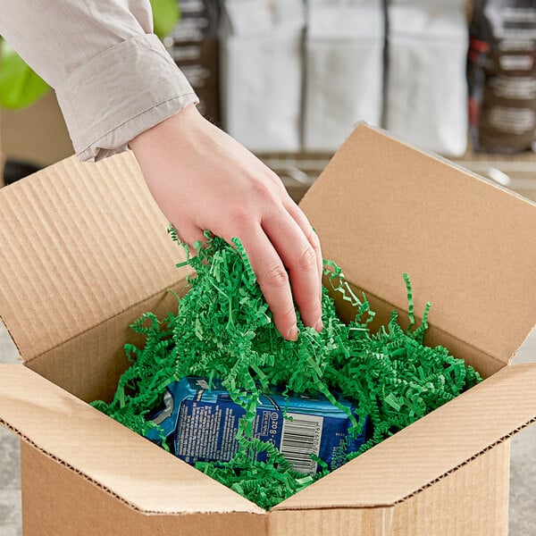 A hand putting Spring-Fill green shredded paper into a cardboard box.