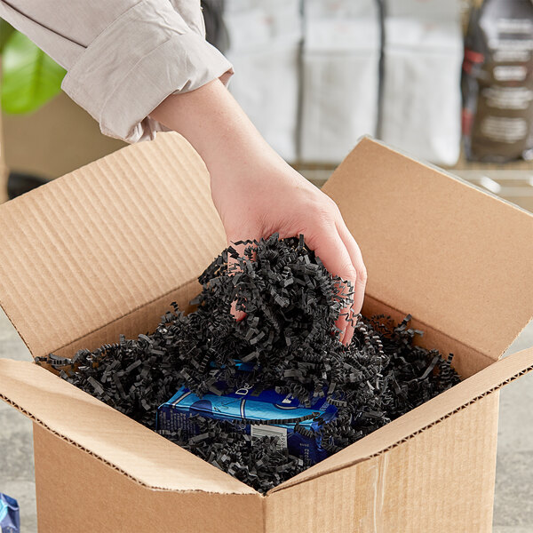 A hand holding a cardboard box with Spring-Fill Black Crinkle Cut paper inside.