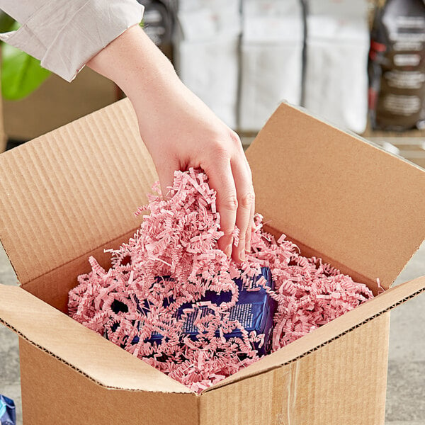 A hand holding a cardboard box with Spring-Fill light pink shredded paper.