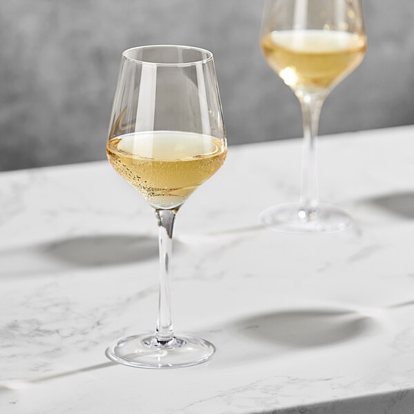 Two Della Luce Astro white wine glasses on a marble table containing yellow liquid.