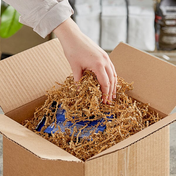 A hand putting Spring-Fill Kraft Crinkle Cut paper shred into a cardboard box.