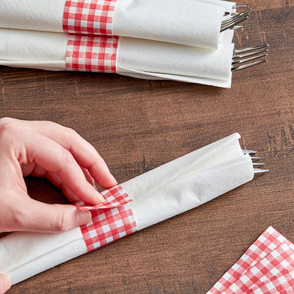 A person's hand using red and white checkered paper to put a napkin on a table.