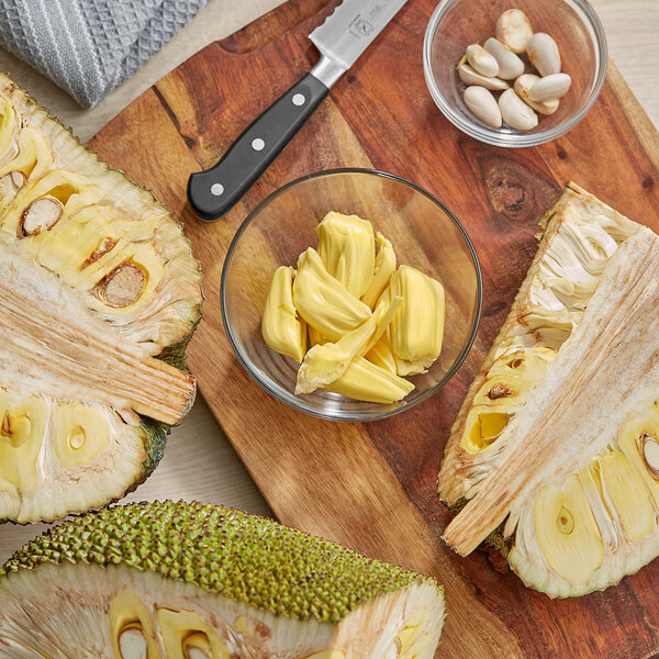 A cutting board with whole jackfruit and a knife on it.
