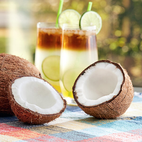 A brown coconut cut in half with coconut water and lime juice in a glass.