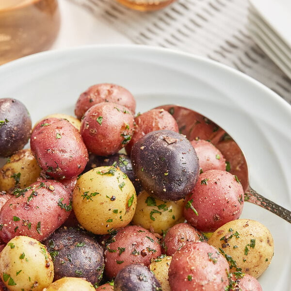 A white plate with red, purple, and yellow marble potatoes on a table with a spoon.