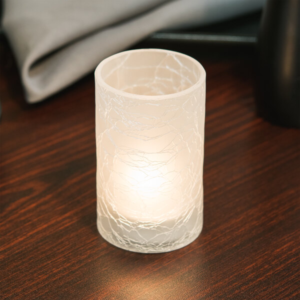 A Sterno Frost Crackle glass candle holder with a lit candle on a table.