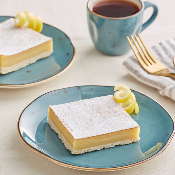 A plate with a Sweet Street Desserts lemon bar square next to a cup of coffee.