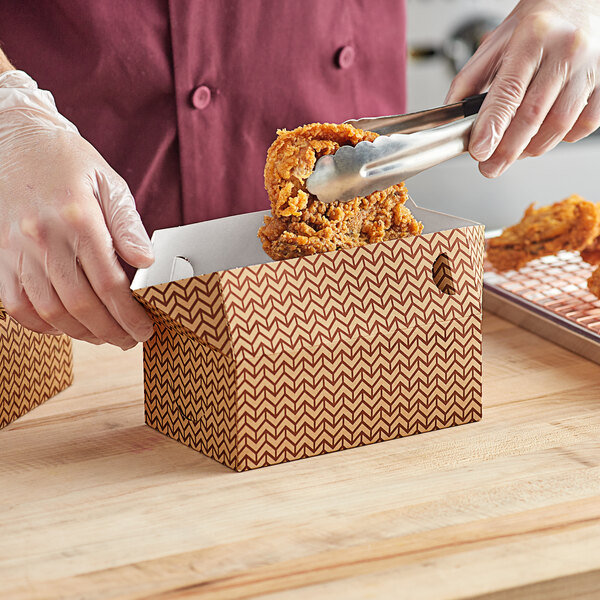 A person using tongs to put chicken in a Choice Cornerstone Take-Out Box.