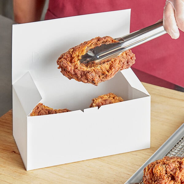 A person holding a piece of fried chicken in a white Choice take-out box.