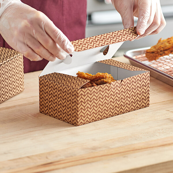 A gloved hand putting fried chicken into a Choice Cornerstone take-out box.