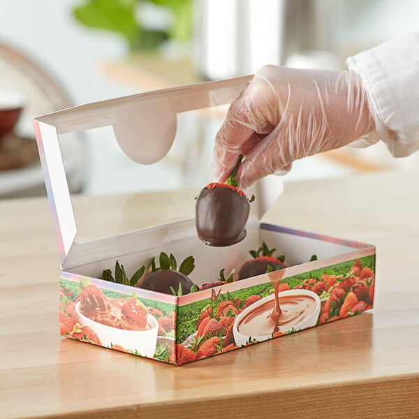A person in gloves holding a 1 lb. windowed chocolate covered strawberry box with chocolate covered strawberries inside.
