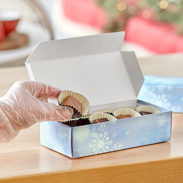 A gloved hand opening a Snowflakes print candy box.