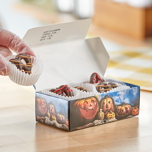 A person holding a Jack-O'-Lantern Halloween print candy box full of chocolate covered pretzels.