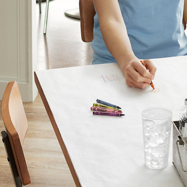 A woman drawing on a white butcher paper table cover on a table.