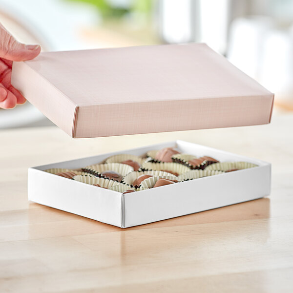 A hand holding a 1/2 lb. pink linen candy box filled with chocolates.